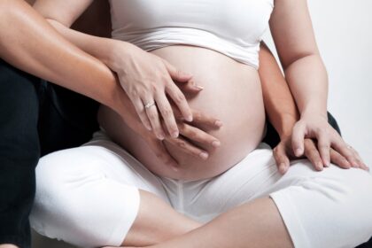 Pregnant woman with husband sitting on floor, holding hands on belly